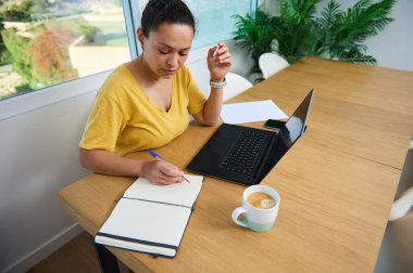 Ahşap bir masada dizüstü bilgisayar üzerinde çalışan profesyonel bir kadın. Serbest çalışmanın, ev ofislerinin ve günlük iş ortamlarının tasviri için ideal.