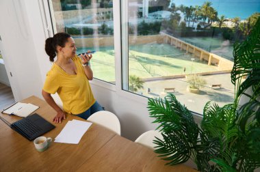 Serbest çalışan bir girişimci, huzur dolu manzaranın tadını çıkararak ev ofisinden çalışıyor. Çoklu görevleri başarıyla yerine getiriyor. Uzaktan kumandalı işleri dengeliyor. Rahat ve verimli bir ortamda kahve molası veriyor..