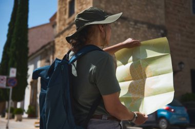 Tarihi bir İspanyol kasabasını keşfeden bir gezgin yön haritası üzerinde çalışıyor. Açık hava maceralarının, kültürel keşiflerin ve bilinmeyen yerlere gitmenin özünü yakalar..
