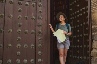 Açık havada gezen bir gezgin, tarihi bir köyü keşfeder, bir harita ve macera duygusu ile donatılmıştır. Büyük ahşap kapılar büyüleyici sahneyi çerçeveler..