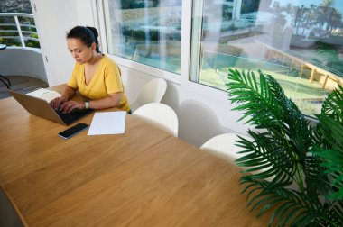 Modern dekor ve parlak bir ortam ile çevrili çağdaş bir ev ofisinde özenle çalışan kadın, üretkenliği, rahatlığı ve girişimci ruhunu simgeliyor..