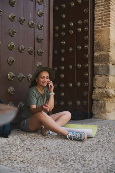 Genç bir gezgin, süslü ahşap bir kapının yanında oturur, harita incelerken, çağrının tadını çıkarır, tarihi mimari ile çevrelenmiş, resimli çevredeki macera ve keşifleri somutlaştırır..