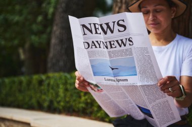 Açık havada otururken metin okumakla meşgul olan şahıs, doğal, sakin bir arkaplanda rahatlama ve bilgilendirici medya tüketimini vurguluyor.