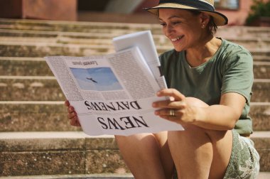 Neşeli orta yaşlı bir kadın, dışarıda güneşin altında merdivenlerde oturup, boş vaktini ve mutluluğunu göstermekten zevk alır..