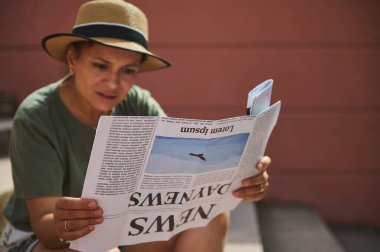 Açık havada gazete okuyan, güneş şapkalı bir kadını resmeden sıradan bir sahne. Bilgilendirme kavramı, eğlence aktiviteleri ve entellektüel bağlılık.