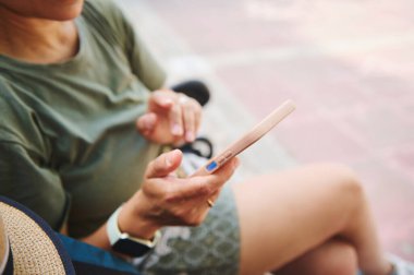 Bir insan açık hava ortamında akıllı telefon kullanarak rahatlarken görülüyor. Sahne, doğal güneş ışığı altında boş zamanlarında teknolojiyle bir bağlantı anı yakalıyor..