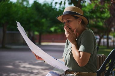 Park çevresinde oturan bir kadın okuduğu bir mektuba şok bir tepki göstererek duygusal yoğunluğunu dile getiriyor..