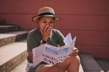 Dışarıdaki taş basamaklarda oturan sıradan giysili bir kadın, şaşırmış ve duygusal bir ifadeyle gazete okuyor. Beklenmedik ya da etkili haberler veriyor..