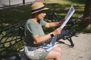 Bir kadın parkta bir bankta otururken gazete okumaktan hoşlanır. Meşgul görünüyor, günlük giysiler giyiyor, hoş bir güneş ışığı altında, sakin bir açık havada..