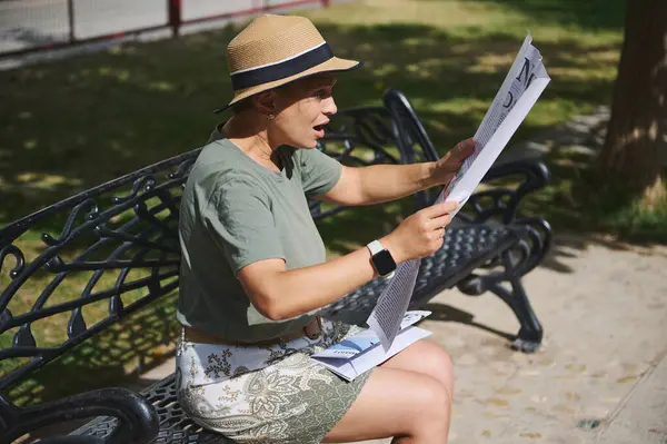 Bir kadın parkta bir bankta otururken gazete okumaktan hoşlanır. Meşgul görünüyor, günlük giysiler giyiyor, hoş bir güneş ışığı altında, sakin bir açık havada..