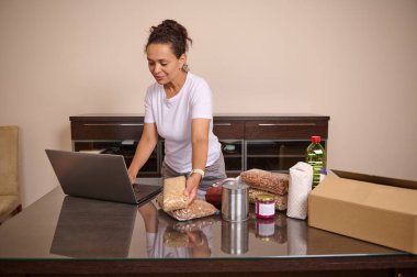 Bir kadın erzak hazırlar ve ev ortamında envanter yönetimi veya yemek hazırlamak için dizüstü bilgisayar kullanır..