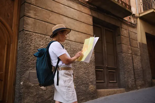 Şapka takan ve günlük kıyafet giyen bir kadın, tarihi bir kentin ilginç sokaklarını keşfederken, kültürel ve mimari hazineler keşfediyor..