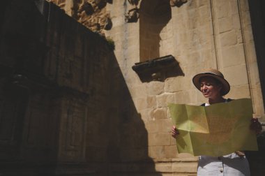 Elinde harita tutan ve tarihi bir şehri keşfeden bir turist kadın. Antik mimari ve seyahat kavramları şehir turu sırasında macera ve keşfi vurguluyor.