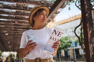 Bir kadın, elinde akıllı telefon ve rehberle pergolas 'ın altında yürüyen tarihi bir bölgeyi keşfediyor. O, büyüleyici ve güneşli bir çevrede gezi yapmaktan hoşlanır..