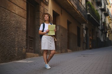 Bir kadın, elinde haritayla eski bir caddeyi keşfetmekten ve mimari güzelliğe hayranlıkla bakmaktan zevk alır..