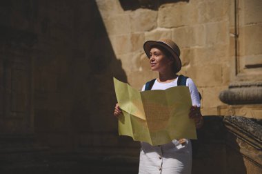Elinde haritası olan meraklı bir turist parlak güneş ışığı altında tarihi bir ortaçağ şehrini geziyor. Keşif, seyahat ve keşif sergiliyor..