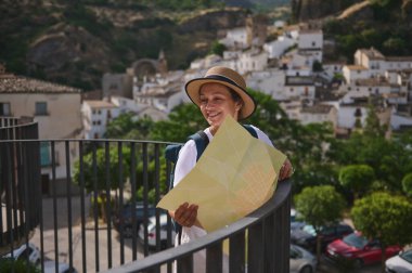 Şapka takan kadın turist elinde harita tutarken, tarihi Akdeniz tepesi köyünün gündüz manzarasının keyfini çıkarıyor..