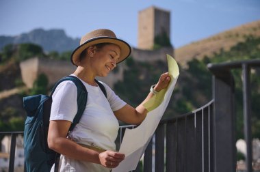 Dişi bir gezgin, elinde çarpıcı bir ortaçağ mimarisi ve doğal manzaralar arasında bir harita tutarak tarihi bir şehir keşfetmekten zevk alıyor..