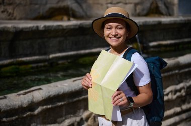 Neşeli bir bayan turist elinde bir harita tutarak gezintiyi, keşfi ve keşif temalarını somutlaştıran seyahat macerası sırasında manzaralı bir yerde geziniyor..
