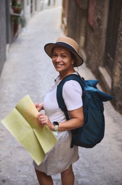 Elinde harita tutan ve tarihi bir ortaçağ şehrinde resim gibi caddeleri keşfeden gülümseyen turist kadın, macera, merak ve kültürel keşiflerin simgesi..