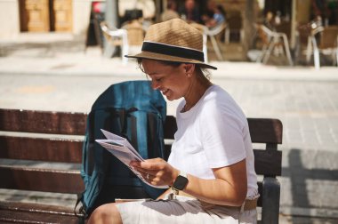Tarihi bir caddede haritayı kontrol eden bir turist kadın. Açık hava kafeleri ve canlı dokularıyla çevrili parlak ve sıcak güneş ışığı altında seyahat deneyiminin tadını çıkarıyor..