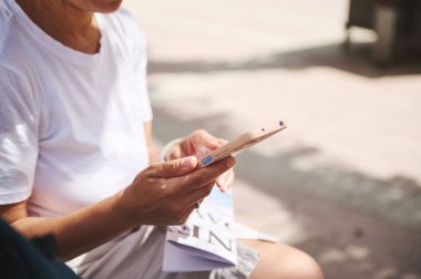 Beyazlar içinde sıradan bir kadın güneşli bir şehirde otururken akıllı bir telefon tutuyor ve günlük yaşamda teknoloji kullanımını vurguluyor..