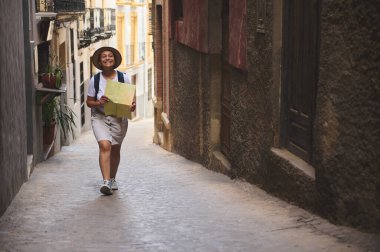 Elinde haritayla gülen bir kadın tarihi bir kasabada kırsal bir ara sokakta yürüyor, yolculuğunun tadını çıkarıyor ve yerel manzaraları keşfediyor..