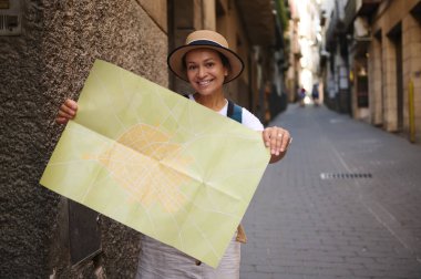 Turistler parlak güneş ışığı altında renkli bir harita tutarak tarihi sokakları keşfediyorlar. Eski şehir yollarını, seyahat noktalarını ve resimli maceraları yeniden keşfet..