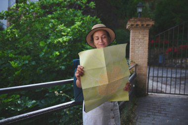 Elinde harita tutan bir kadın, küçük caddeleri ve yemyeşil yeşillikleri olan pitoresk bir çevrede yeni bir varış yeri keşfederken, rahat bir yolculuğun tadını çıkararak büyüleyici bir tarihi alanı keşfediyor..