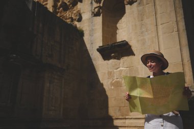 Elinde harita tutan ve tarihi bir şehri keşfeden bir turist kadın. Antik mimari ve seyahat kavramları şehir turu sırasında macera ve keşfi vurguluyor.