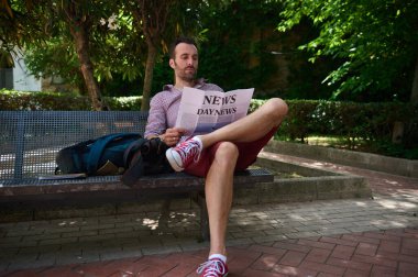 Rahat bir adam rahatça bir bankta uzanır, ağaçların gölgesinde bir gazete okur, huzurlu bir bahçe ortamında, huzur ve rahatlık taşır..