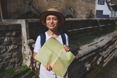 Şapka takan bir kadın elinde haritayla tarihi sokakları keşfediyor. Etrafında eski bir mimari ve büyüleyici bir çeşme var. Macera ve seyahat ruhunu çağrıştırıyor..