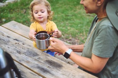 Açık hava pikniğinde bir çocuk ve yetişkin sıcak içeceklerle bağ kurar, aileyi, arkadaşlığı ve doğayı takdir eder..