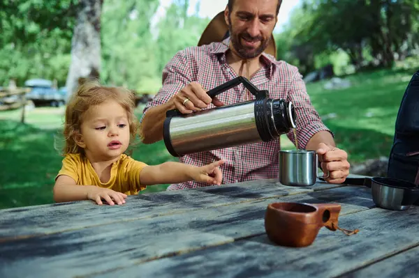 Bir baba ve çocuk, park gezisi sırasında ortak bir anın tadını çıkarırlar. Baba, doğayla ve yeşilliklerle çevrili, çevre dostu ve açık hava yaşam tarzıyla çocuğun eğlenmesi için bir içki koyuyor..