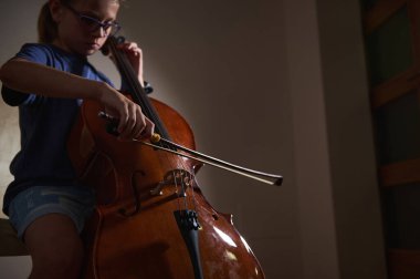 Odaklanmış genç bir çello sanatsal bir ortamda yayları tellere çizen genç bir çellocu. Atmosferik ışıklandırmada müzik pratiği ve tutku vurgulanıyor.