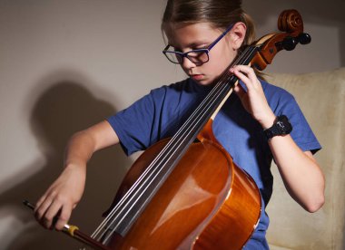 Genç kız yoğun bir şekilde çello çalışıyor, konsantrasyonunu ve müziğe olan aşkını gösteriyor. Yakın çekim, doğal ışıklandırma sıcak bir atmosfer yaratır. Gençlik, müzik ve adanmışlık konuları için ideal.