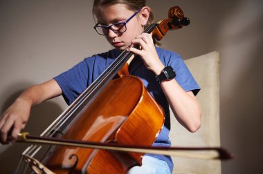 Genç bir birey dikkatle çello çalarken görülüyor, performanslarında ustalaşmaya odaklanıyor. İçerideki sıcak ortam, müziğe olan bağlılıklarını ve sevgilerini vurguluyor..