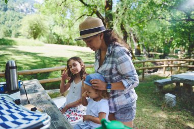Güzel bir parkta, yemyeşil ağaçlarla çevrili ve piknik alanında temiz hava ve dinlenmenin tadını çıkaran bir aile..