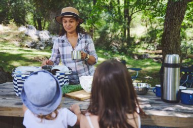 Bir aile açık havada birlikte güzel vakit geçirir. Yeşillik ve güneş ışığıyla pikniğin tadını çıkarırlar..