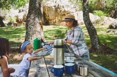 Bir aile, doğal, dingin bir arka planı olan ve ağaçlar ve yeşillik barındıran bir ormanda piknik yaparken dışarıda vakit geçirmekten zevk alır..