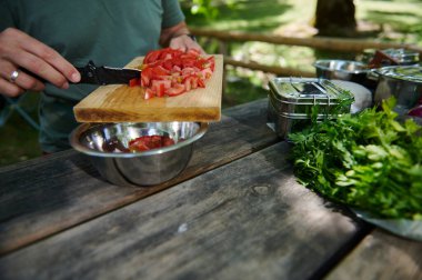Bir insan, etrafını otlar ve metal kaplarla çevrili, tahta bir tahtada taze domatesleri dilimliyor. Al fresk pişirmenin ve doğanın cömertliğinin özünü yakalıyorum..