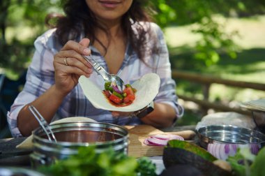 Bir insan açık hava ortamında taze sebze kullanarak lezzetli bir taco hazırlıyor. Piknik düzeninde canlı renkler ve toprak atmosfer var. Al fresco yemeği için mükemmel..