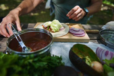 Açık hava piknik seti, soğan, marul, sos tenceresi ve avokado ile taze bir paket hazırlayan bir elin gösterimi, yaz pikniği yemekleri ve sağlıklı yemek hazırlıklarını betimliyor..