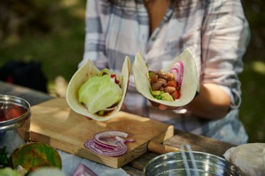 Açık hava piknik ortamında içi taze sebzelerle dolu bir çift tortilla sergileniyor. Parlak doğal ışık, sağlıklı içeriği, sıcaklığı ve sağlık bilinci olan atmosferi arttırır..
