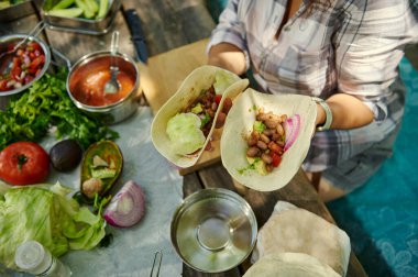Gevşek bir açık hava yemeği hazırlama sırasında sebze ve salsa da dahil olmak üzere canlı malzemelerle dolu bir masanın üzerinde duran taze tacolar..