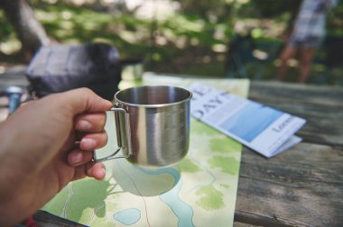 Haritaların yanında tutulan paslanmaz çelik bardak ve ahşap bir masanın üzerinde duran eşyalar, doğa kampının ve keşiflerin özünü doğal bir ortamda yakalıyor..