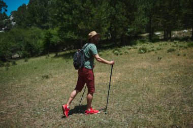 Gezgin, yürüyüş direkleri ile yemyeşil bir ormanı keşfediyor, açık hava kıyafetleri giyiyor, doğal ve sakin bir çevrede macera ve açık hava keşfi ruhunu yakalıyor..