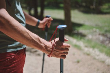 Güneşli bir açık havada yürüyüş yaparken direklere tutunan ve aktif ve maceralı bir yaz yaşam tarzını vurgulayan bir insanın yakın plan görüntüsü.