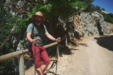 Yazın güneşli kayalık bir patikada yürüyüş yapan bir adam açık hava macerasının ve keşiflerin özünü yakalıyor. Aktif bir yaşam tarzını yansıtan doğal bir araziyle kaplıdır..