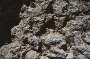 Yakın plan bir fotoğraf. Karmaşık dokular ve kaya yüzeyinin engebeli özellikleri, doğal oluşumu vurguluyor ve jeolojik olarak ilginç detaylar gün ışığıyla geliştiriliyor..